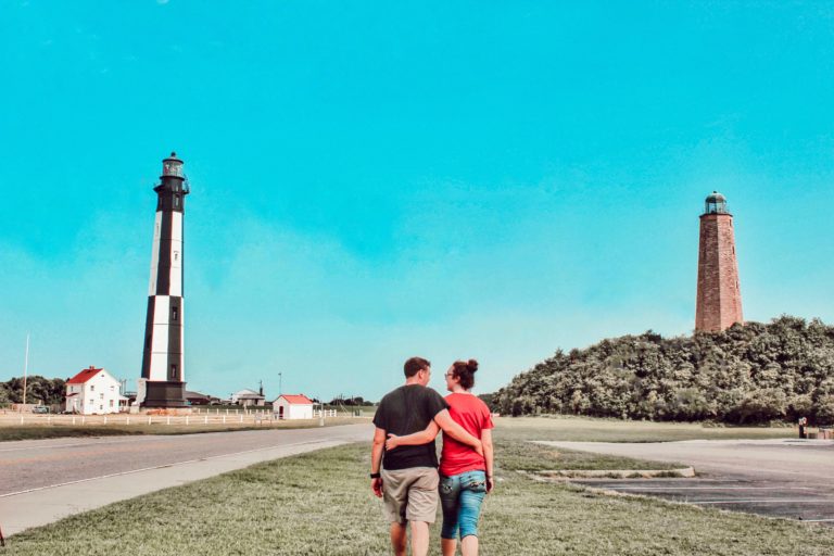 a couple in the middle of a field walking towards Cape Henry Lighthouse