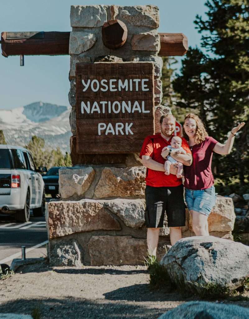 couple with baby standing in front of the Yosemite National Park sign in Tuolumne meadows. the best Yosemite entrance for the summer.