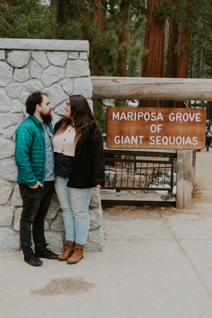 Gina and Victor, a couple, standing in front of the sign for the Mariposa Grove of Giant Sequoias in Yosemite National Park. 